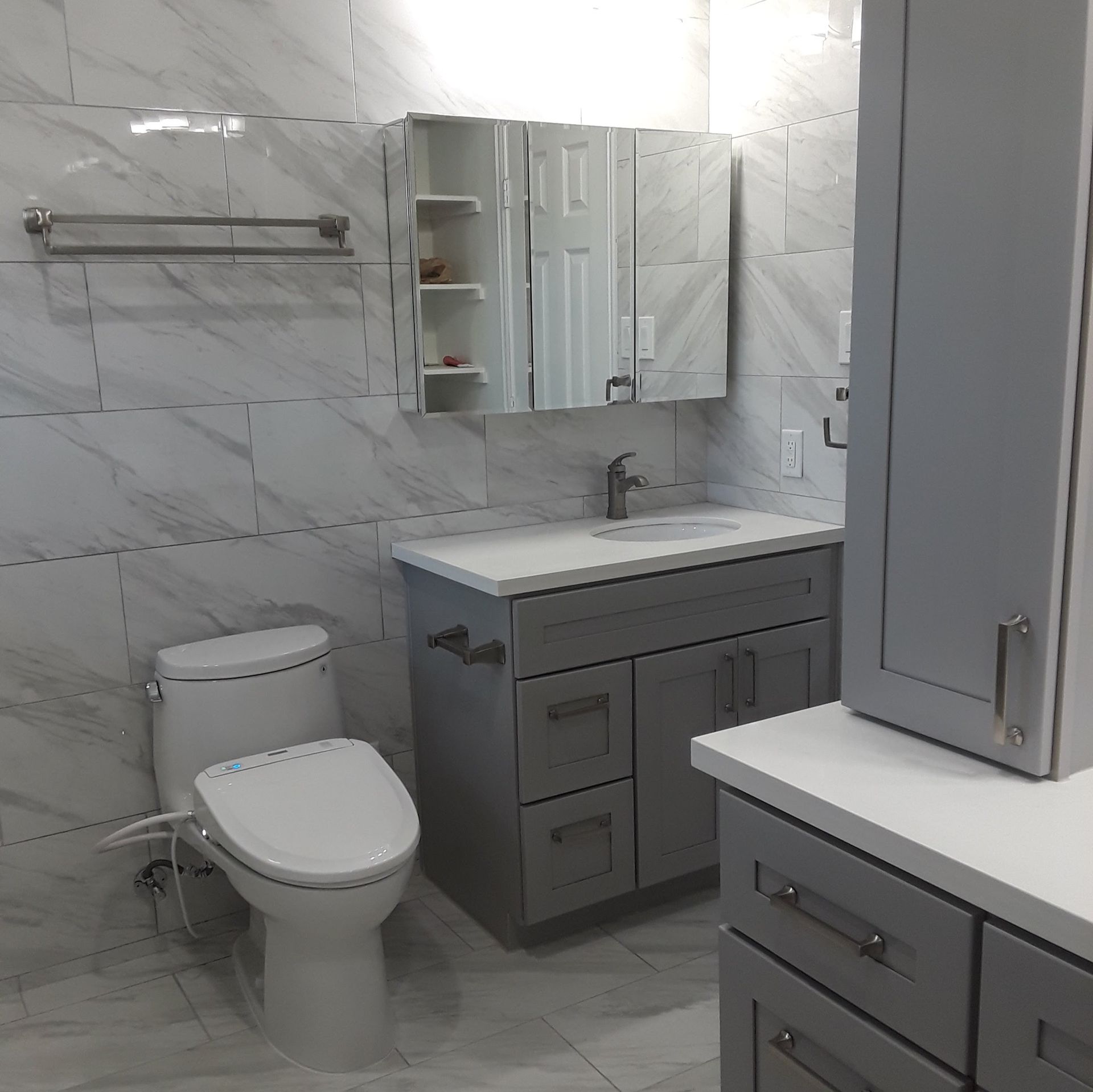 Gray and white bathroom with toilet, vanity, and cabinets. Marble tile walls.