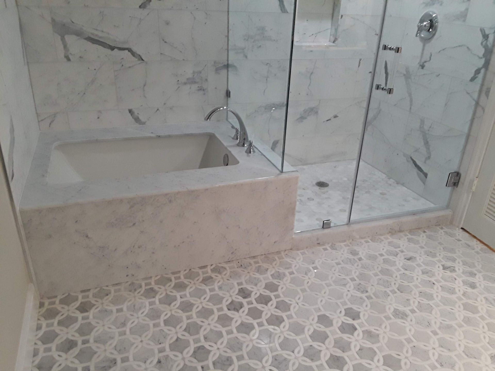 Luxurious bathroom with marble walls and mosaic tile floor, featuring a built-in tub and glass shower enclosure.