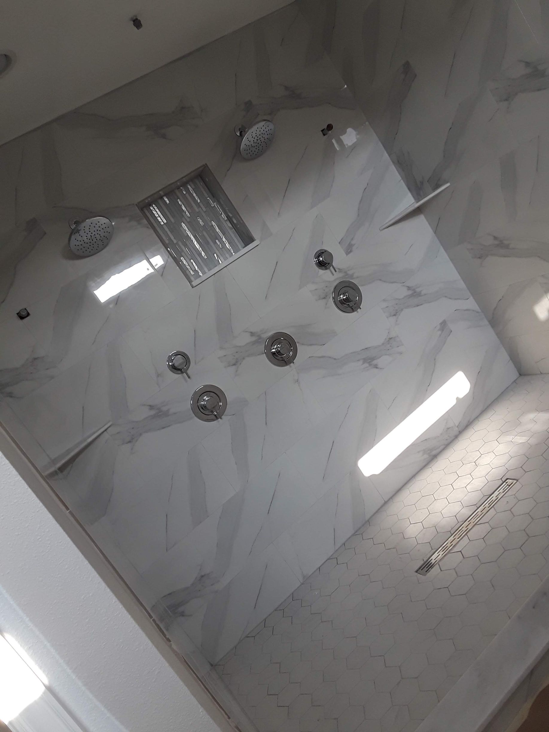 Luxurious tiled shower with multiple showerheads and a recessed shelf.