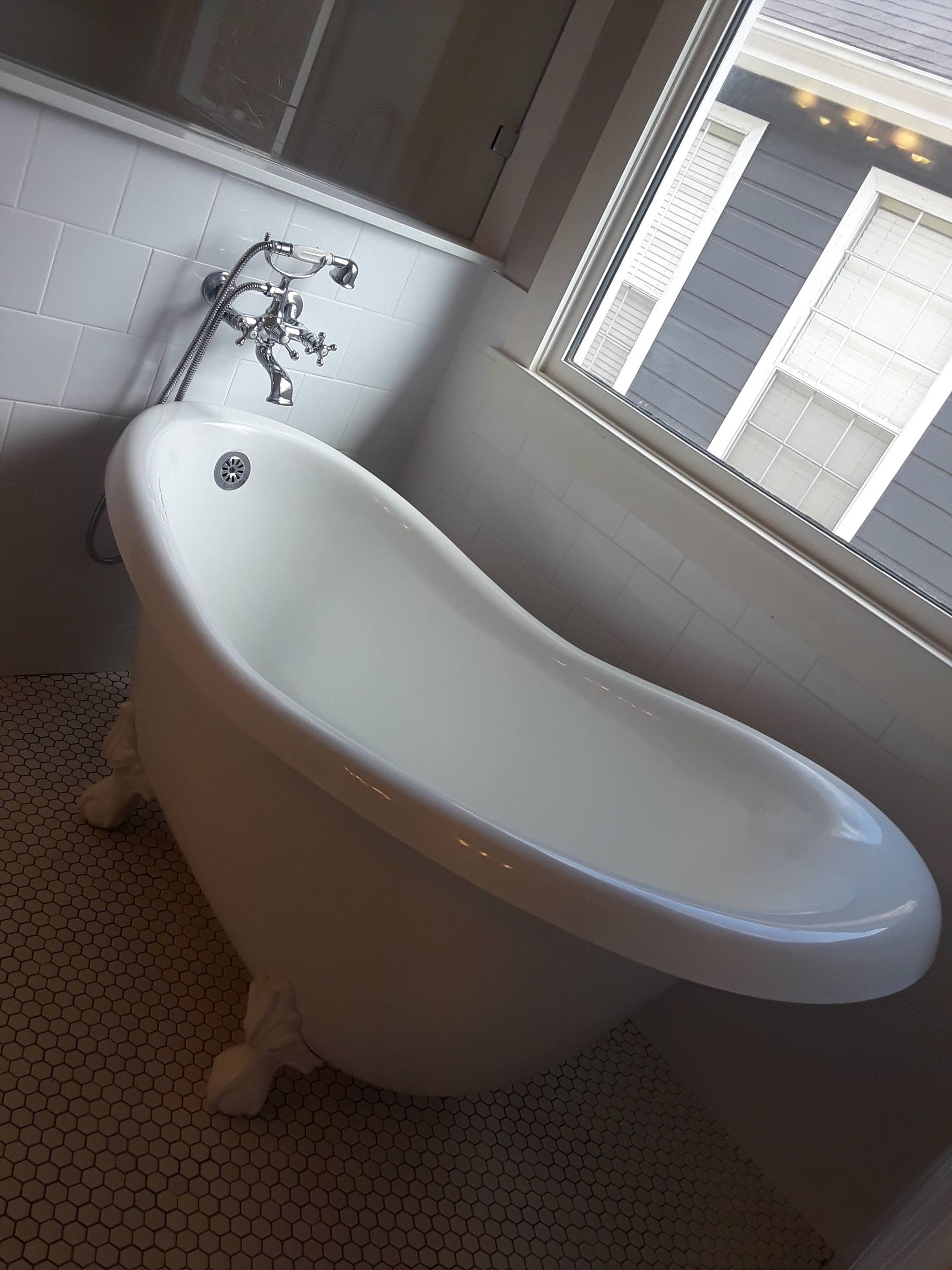 Clawfoot bathtub in a bathroom, white with ornate faucet and window.