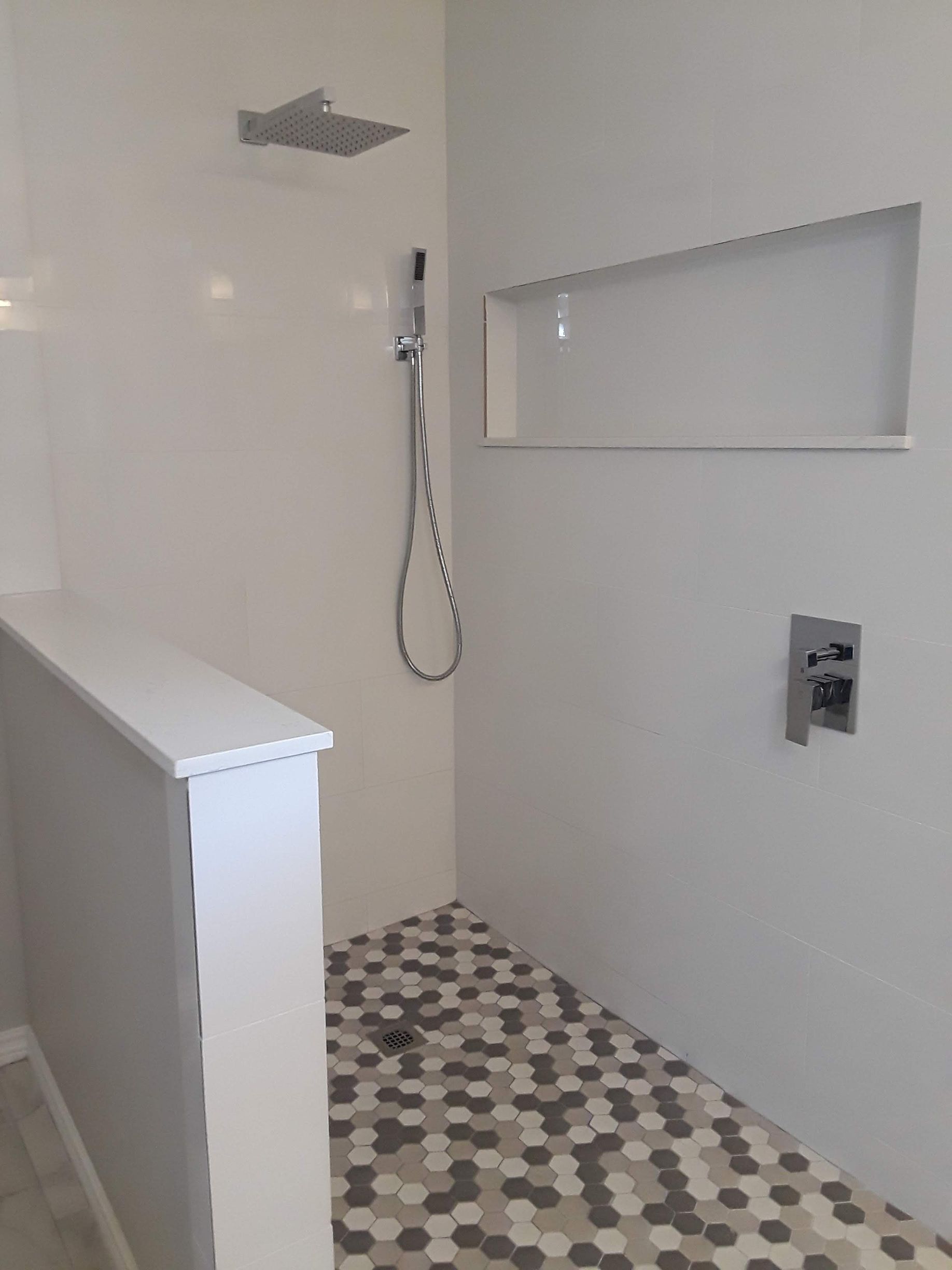 Modern shower with white walls, hexagon tile floor, built-in shelf, and chrome fixtures.