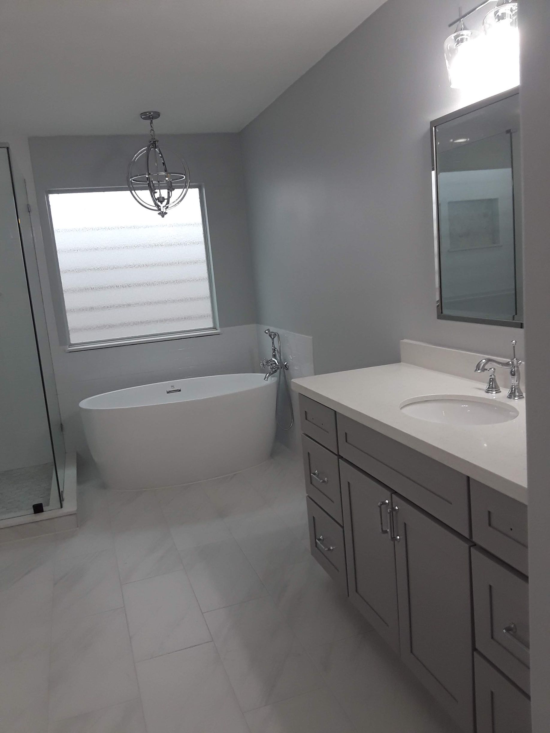Bathroom with a white freestanding tub, gray vanity, and a window with white blinds.
