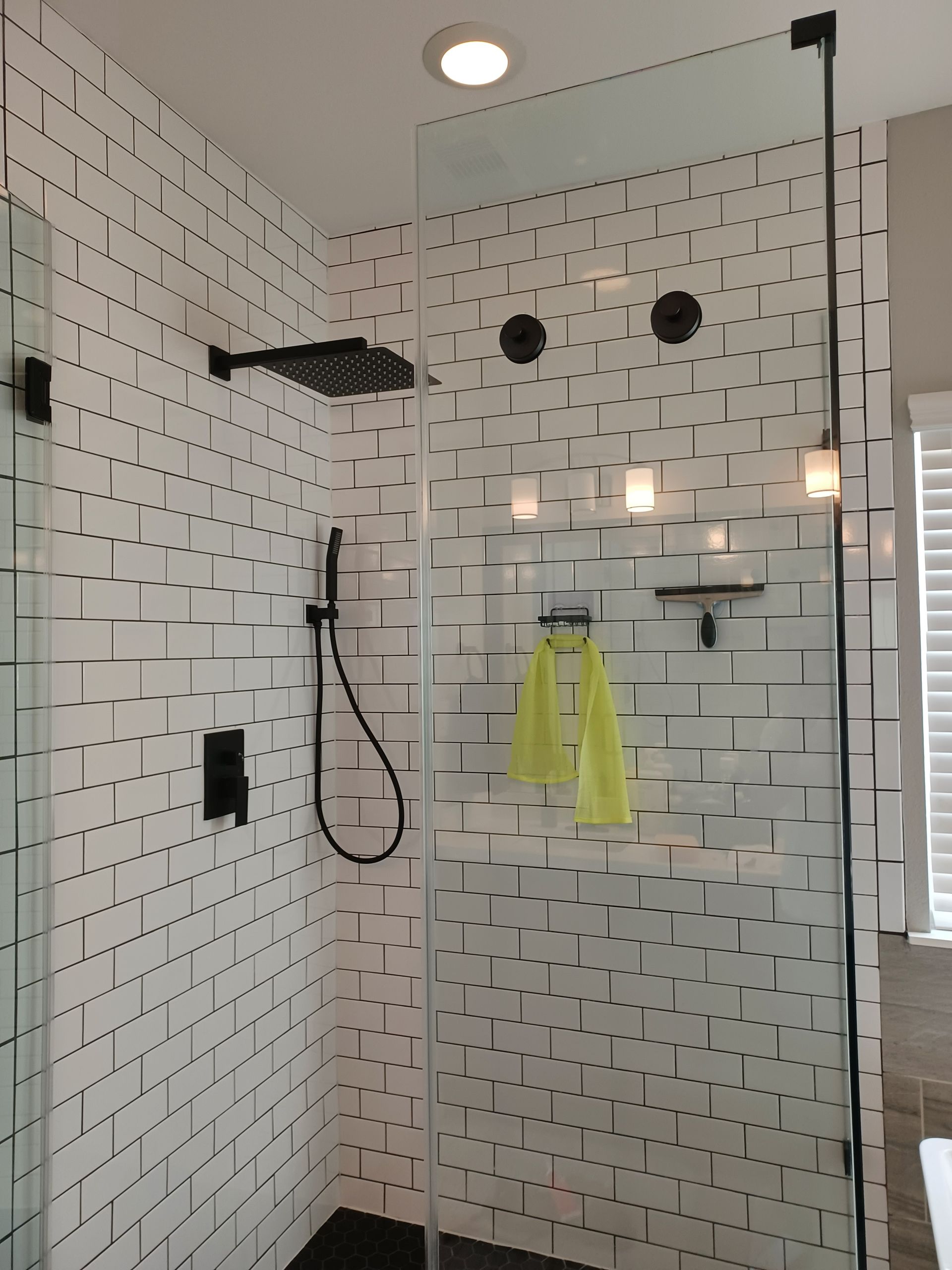 Modern shower with white tiled walls, black fixtures, and glass door.