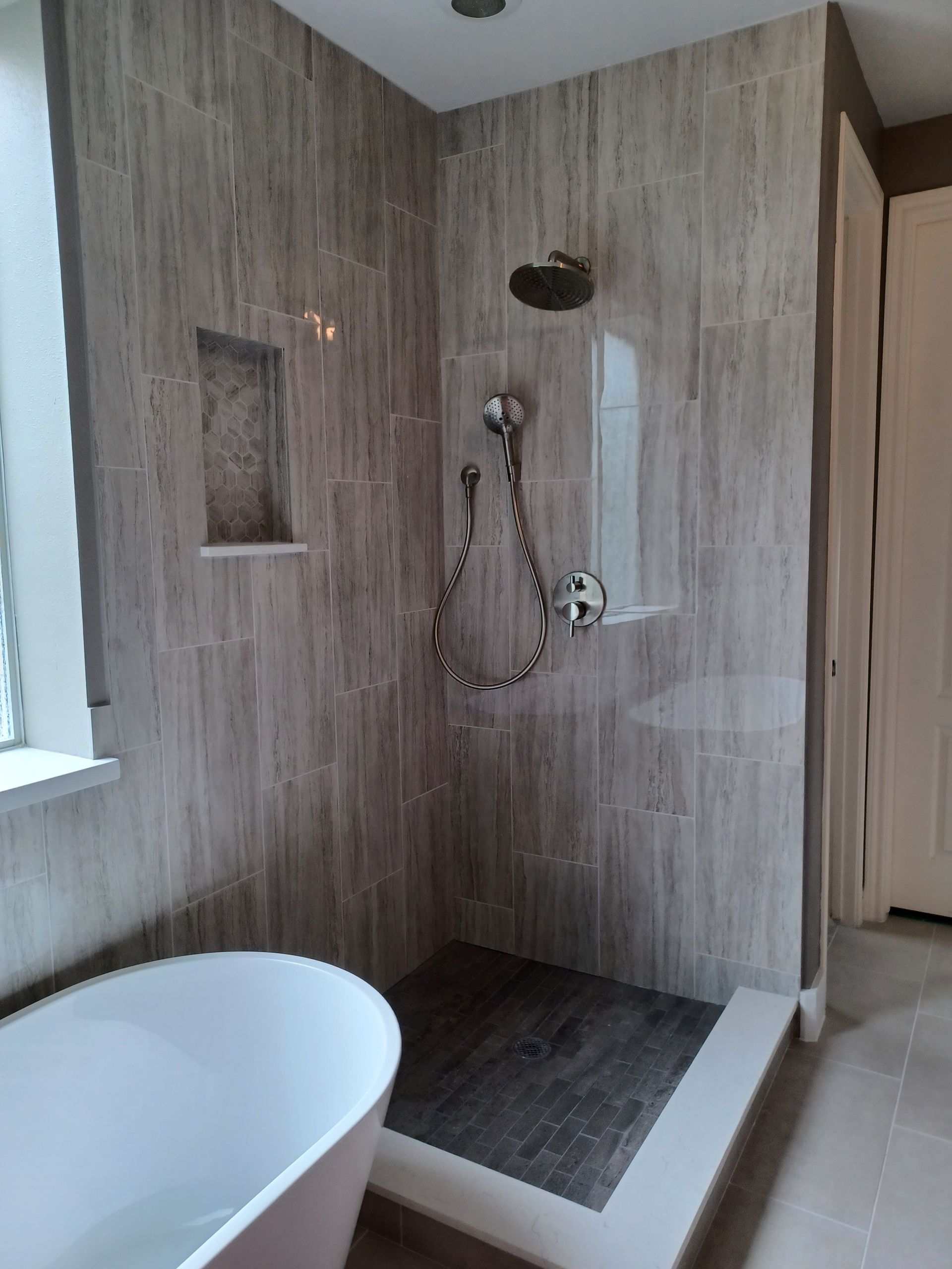 Modern bathroom with gray tiled shower and freestanding tub.