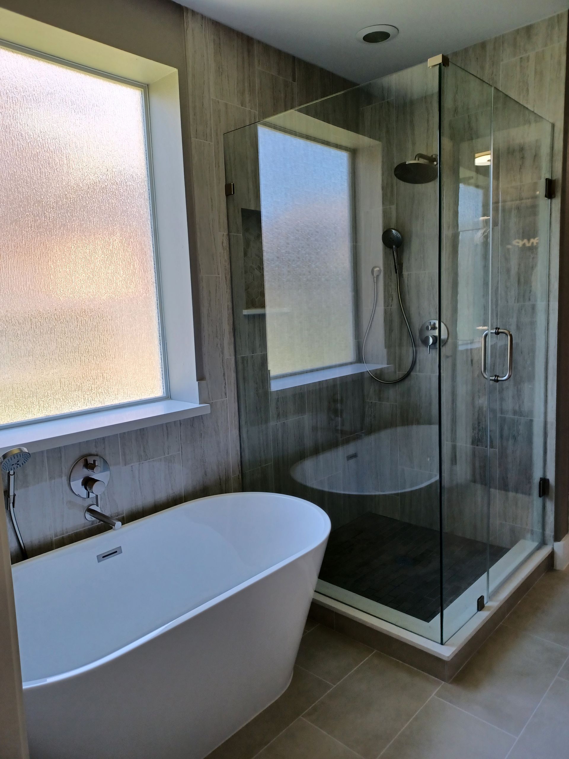 Modern bathroom with a freestanding tub, glass shower, and textured gray walls.
