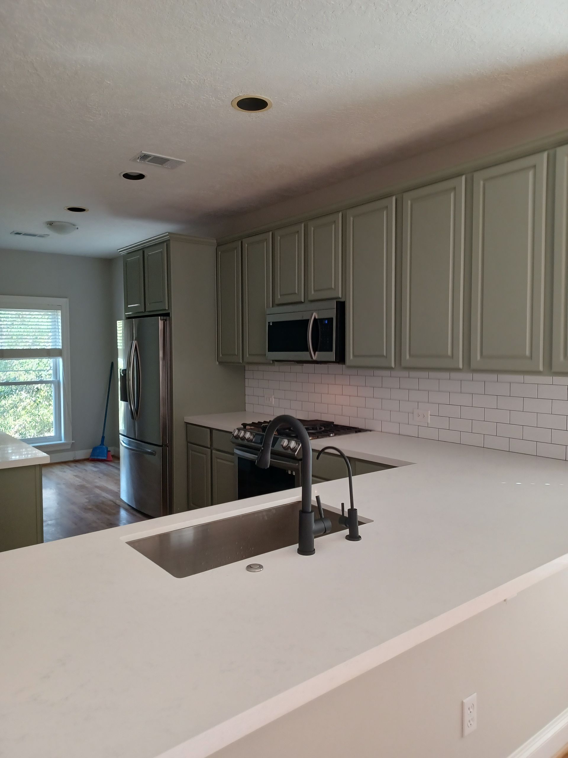 Kitchen with light green cabinets, white countertops, stainless steel appliances, and a black faucet.