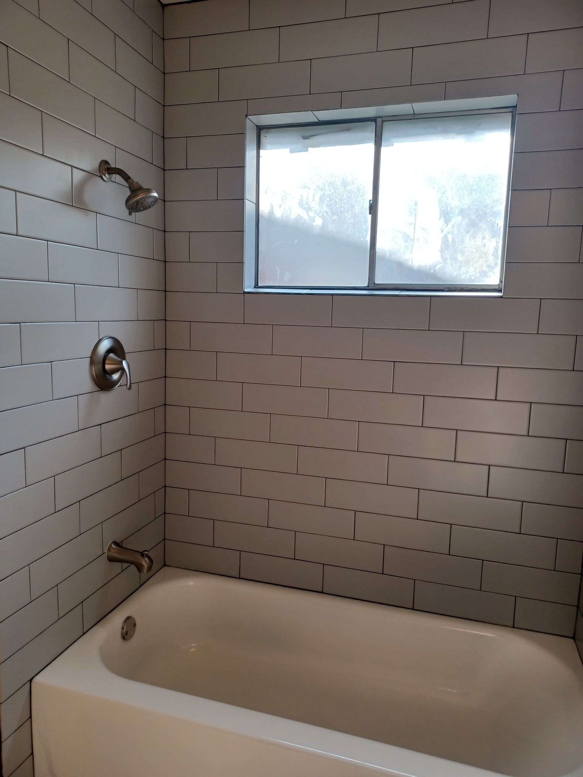 Bathroom with white subway tile, a bathtub, showerhead, and window.