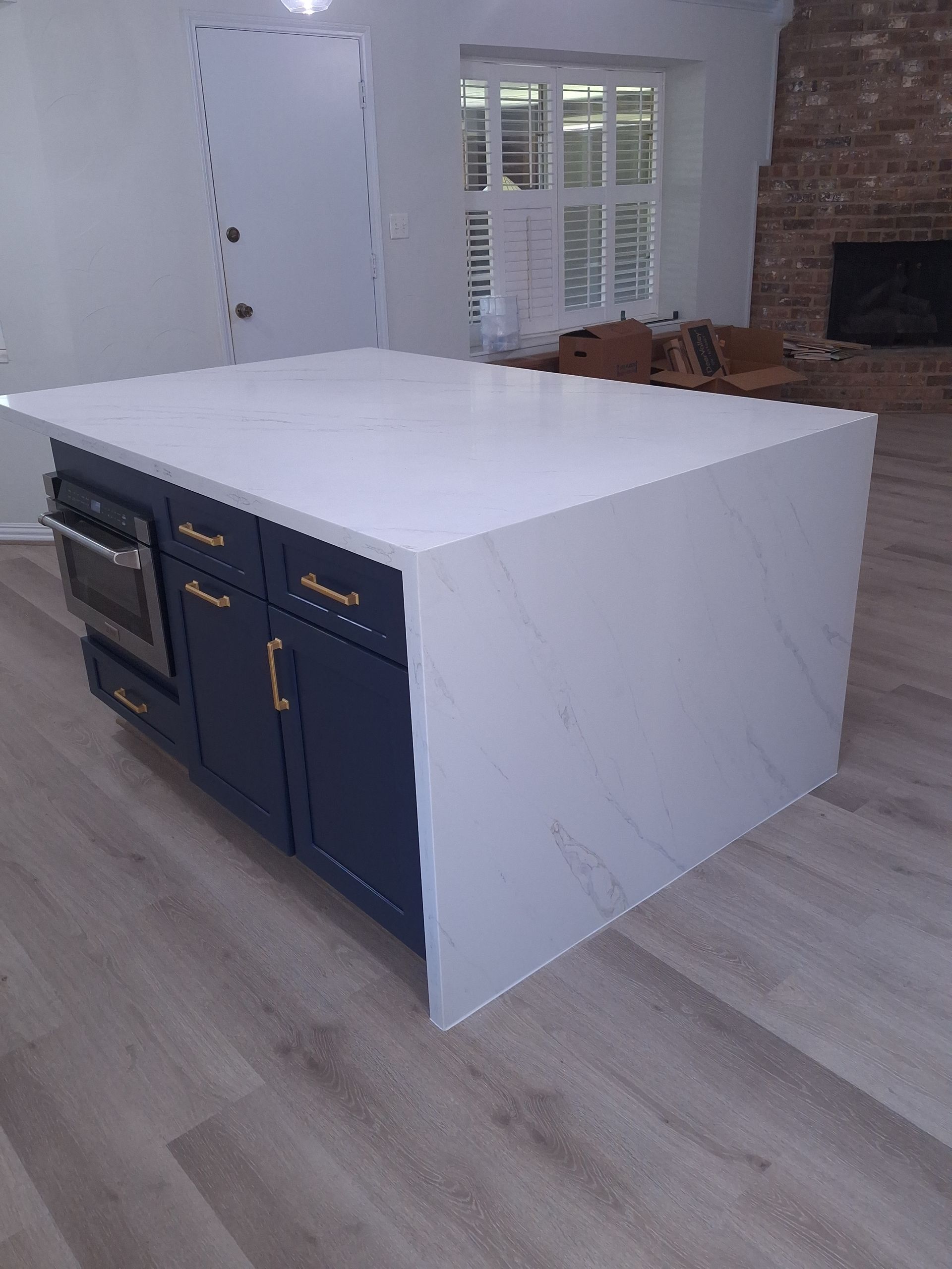 Blue kitchen island with white countertop, built-in oven, and gold hardware in a room with hardwood floors.
