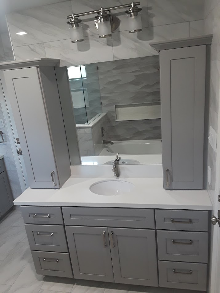 Gray bathroom vanity with sink, mirror, and two tall cabinets. Modern design with light fixtures above.