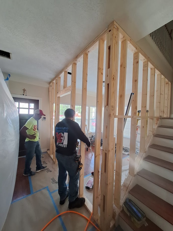 Kitchen under construction; bare island and cabinets, windows, white walls.