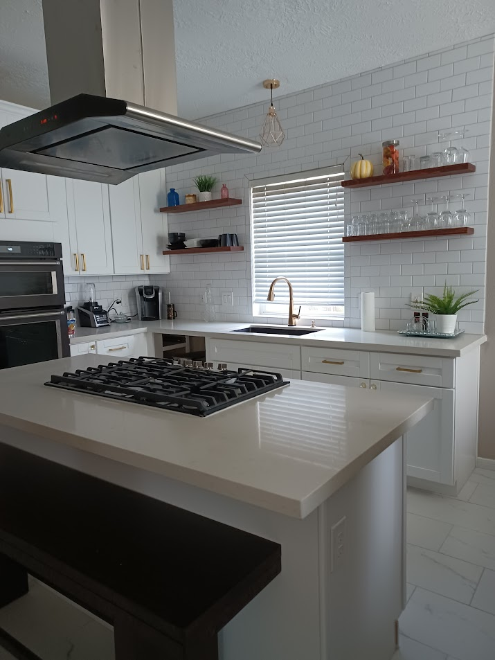 Bright, spacious kitchen with large white island, wooden beams, and windows overlooking a lush green yard.
