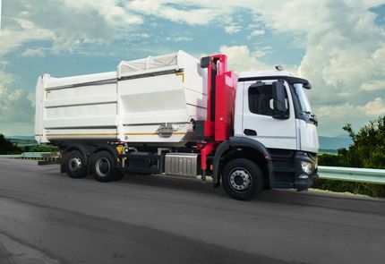 Un camion della spazzatura bianco e rosso su una strada contro un cielo nuvoloso.