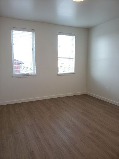 An empty room with hardwood floors and three windows.