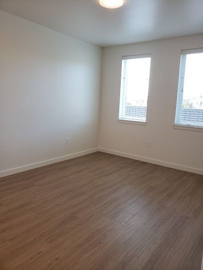 An empty bedroom with hardwood floors and two windows.