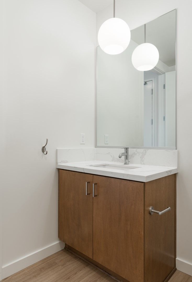A bathroom with a sink , mirror and wooden cabinets.
