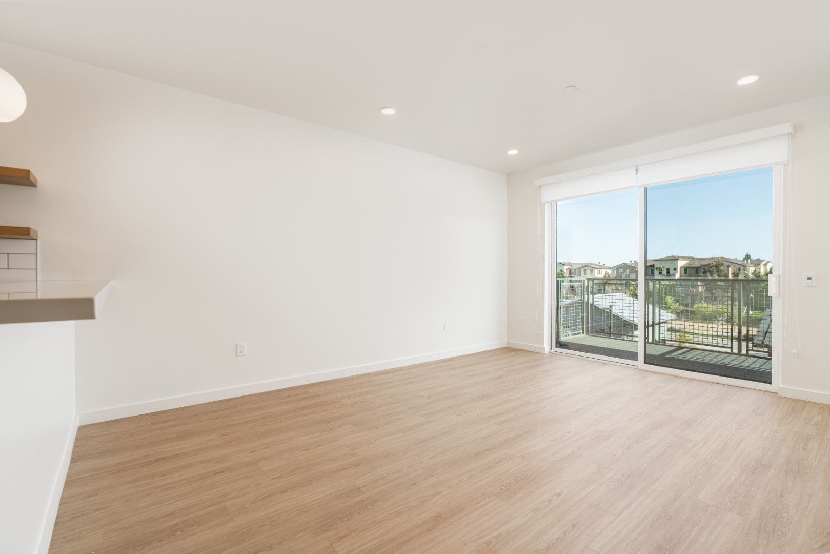 An empty living room with hardwood floors and sliding glass doors leading to a balcony.