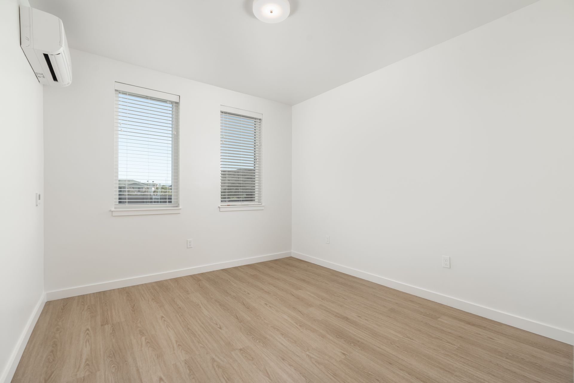 An empty room with hardwood floors and two windows.