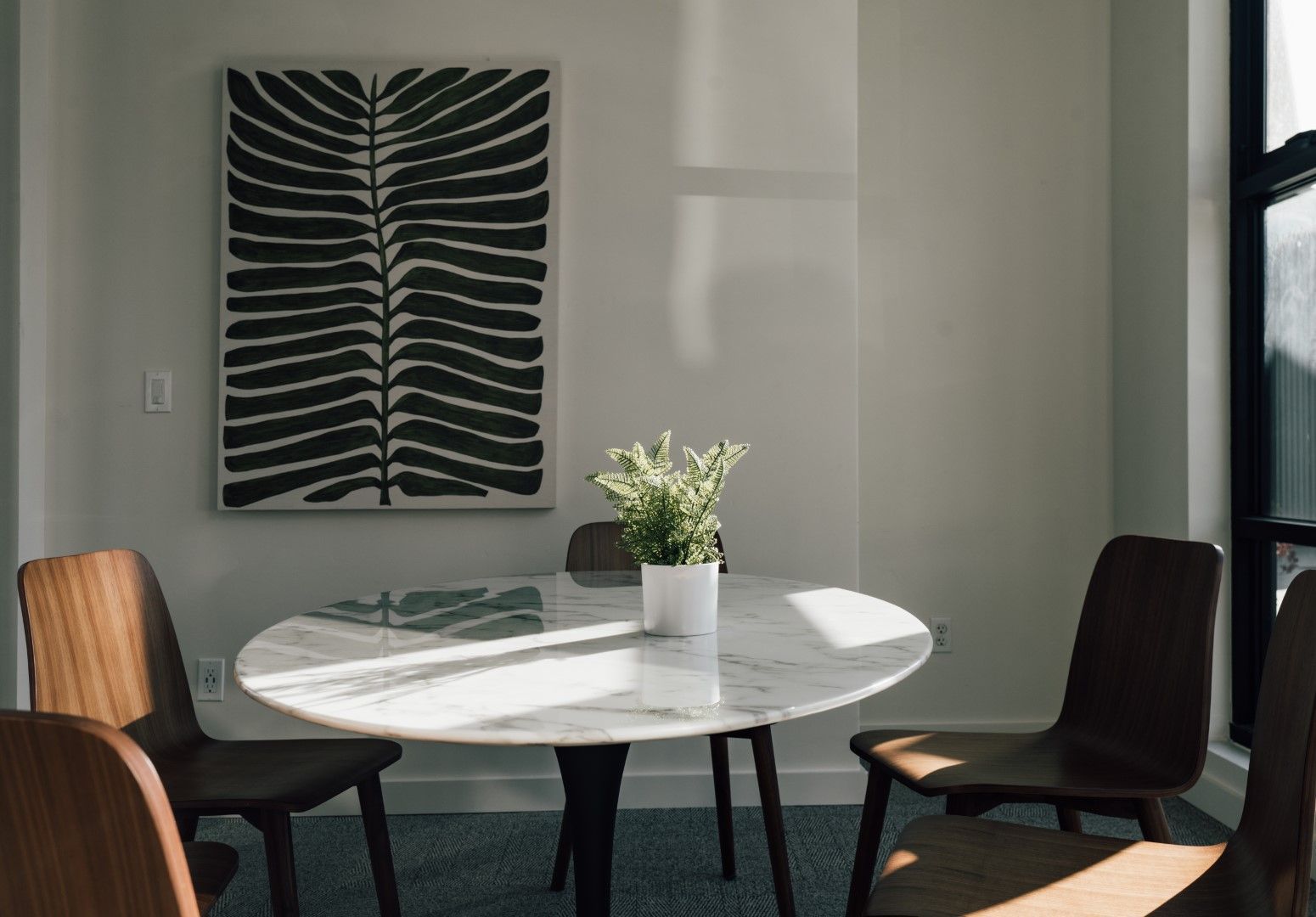 A dining room with a round table and chairs and a painting on the wall.