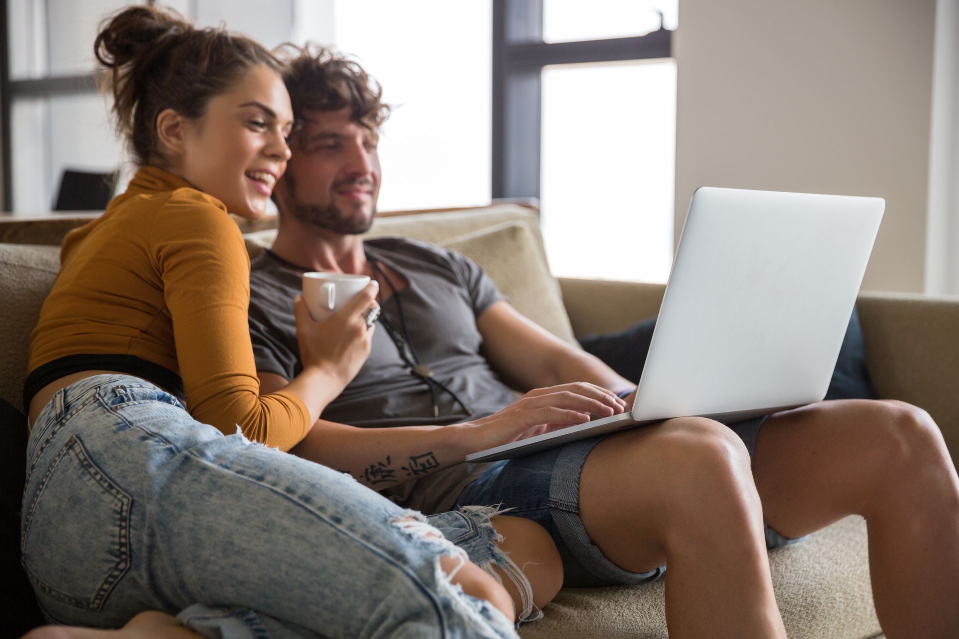 A man and a woman are sitting on a couch looking at a laptop.