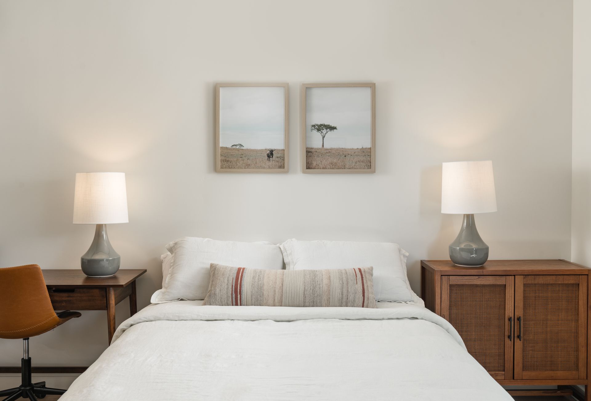 A bedroom with a bed , two lamps , a desk and two pictures on the wall.