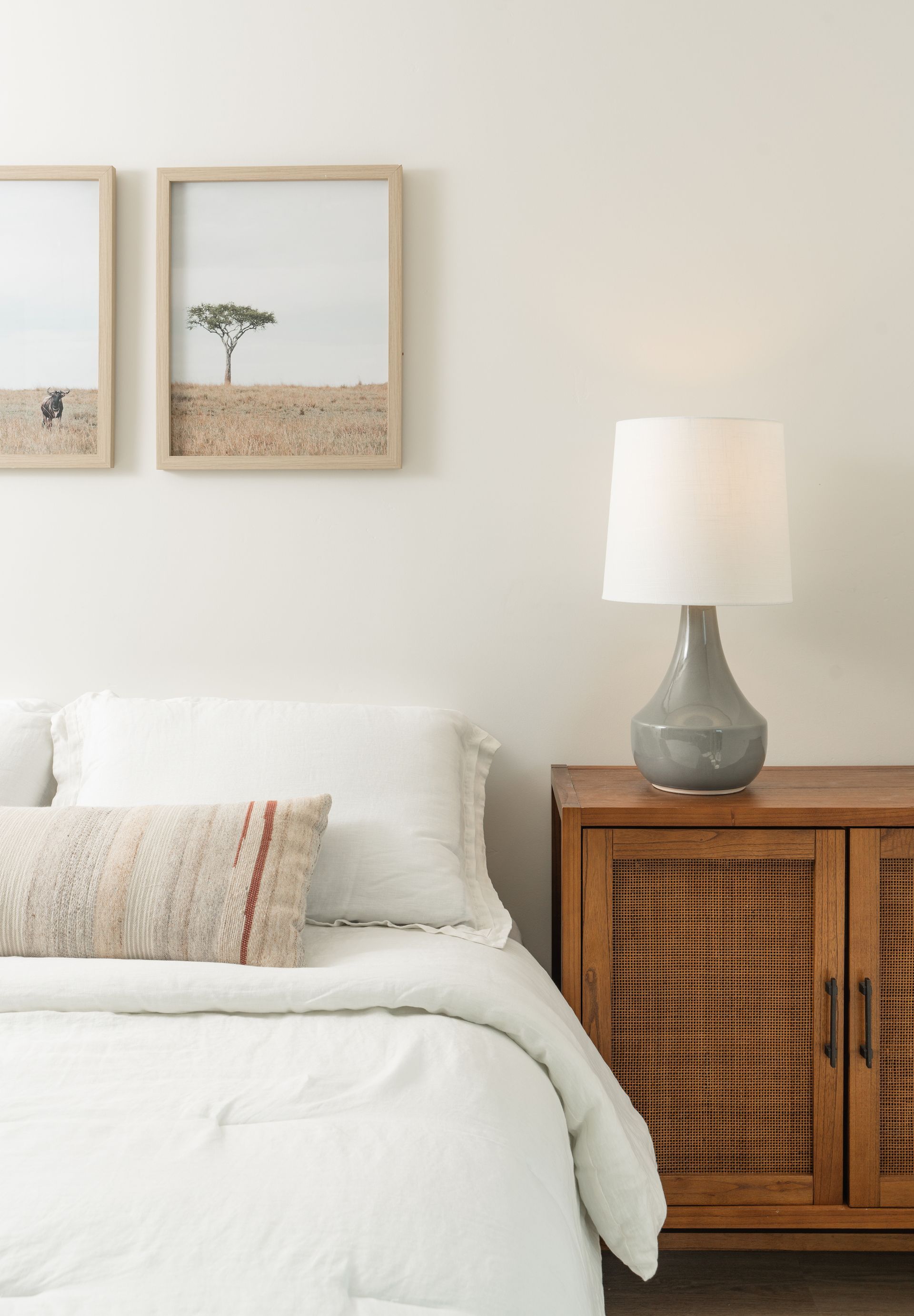 A bedroom with a bed , nightstand , lamp and two pictures on the wall.