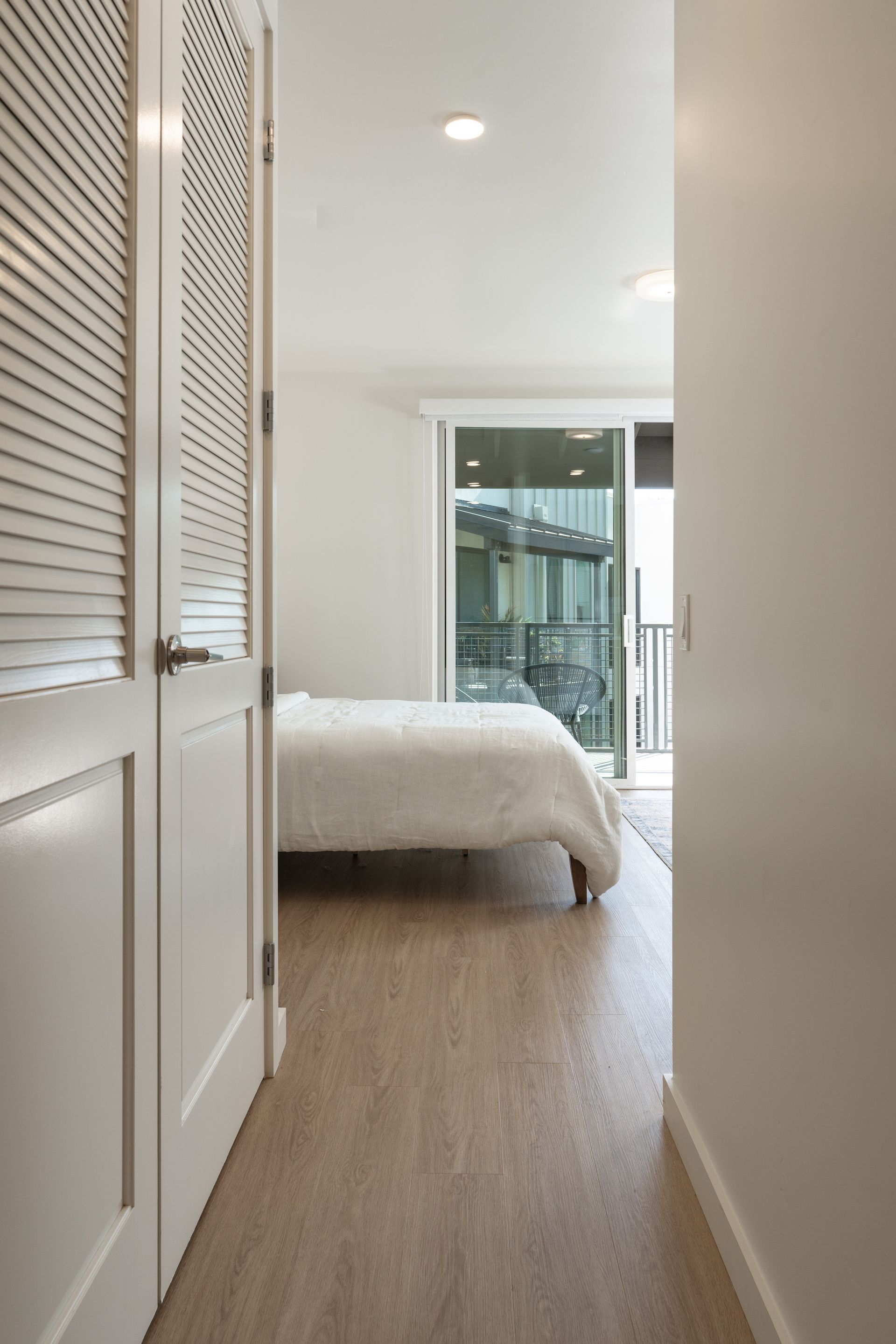 A hallway leading to a bedroom with a bed and a sliding glass door.