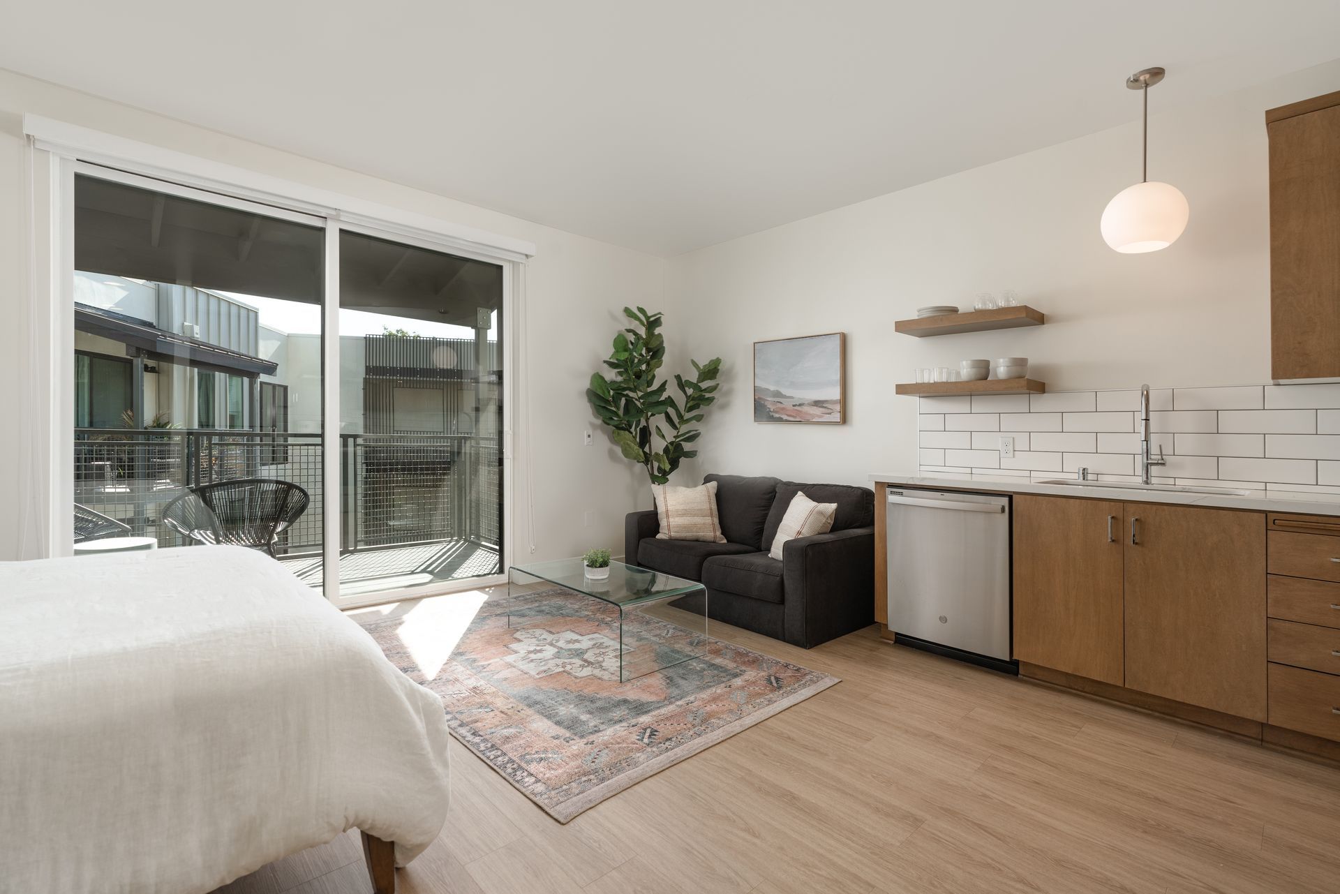 A living room with a couch , a bed , a kitchen and a balcony.