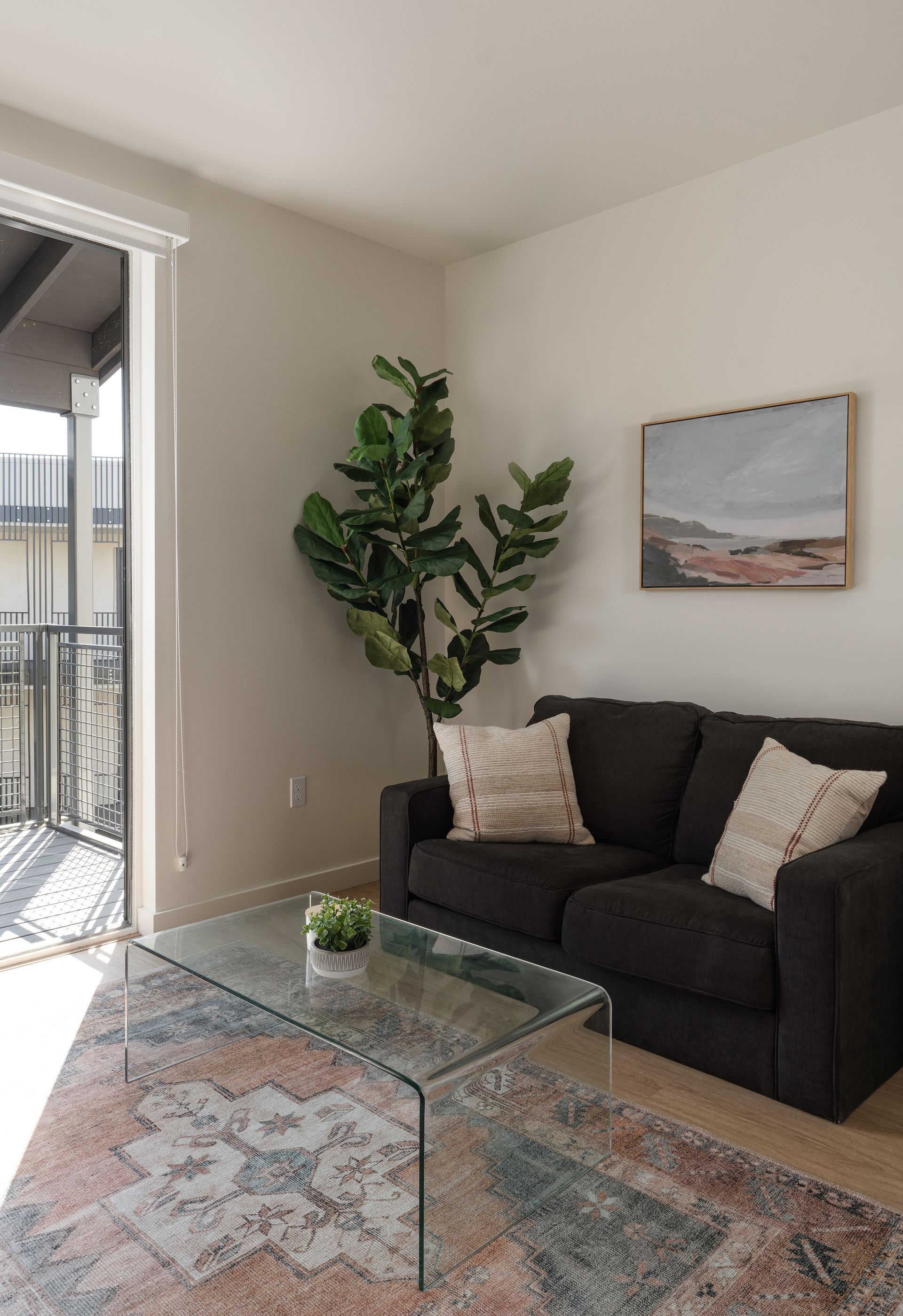 A living room with a black couch and a glass coffee table.