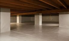 An empty basement with white pillars and a wooden ceiling.