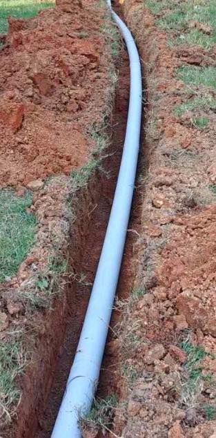 A white pipe is laying in the dirt in a trench.