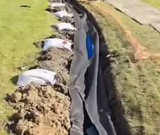 A row of sandbags are lined up on the side of a dirt road.