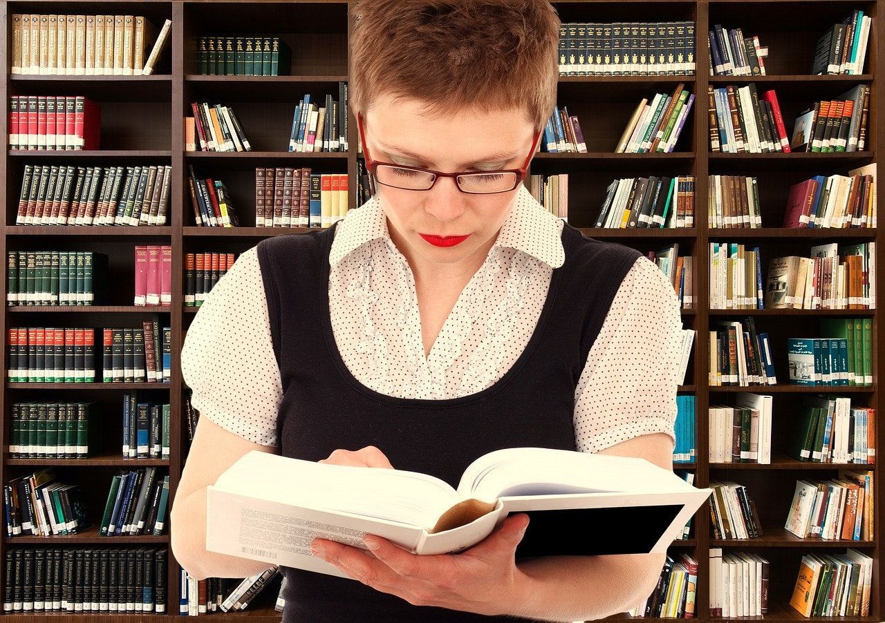 A woman wearing glasses is reading a book in a library