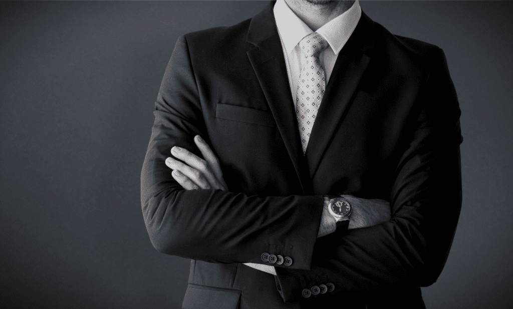 A man in a suit and tie is standing with his arms crossed.