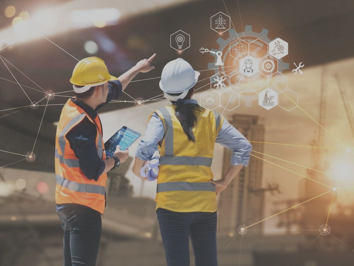 Two individuals standing in safety vests and hard hats pointing  with analysis and diagnosis graphics. 