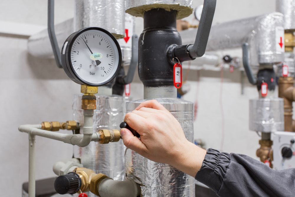 A Person is Adjusting a Pressure Gauge on a Pipe in a Boiler Room — Chad Warrington Plumbing In Salamander Bay, NSW