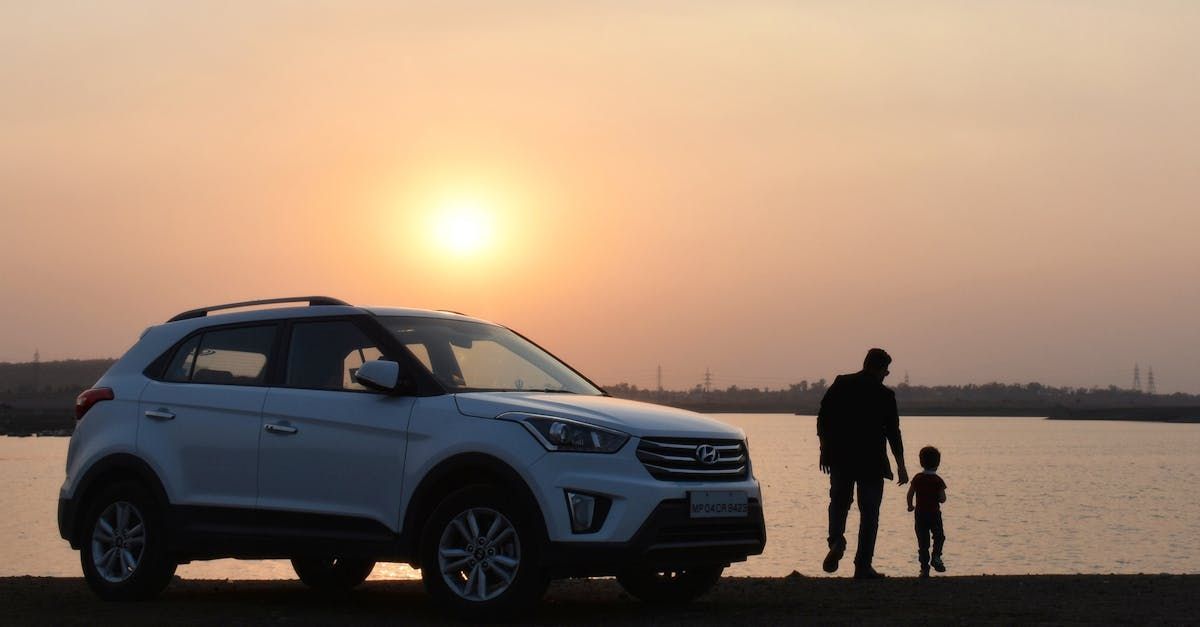 A man and a child are standing next to a car on the beach at sunset.