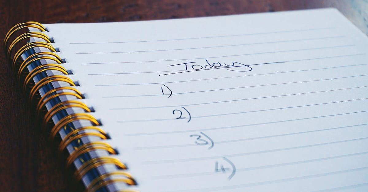 A spiral notebook with a list written on it is sitting on a wooden table.