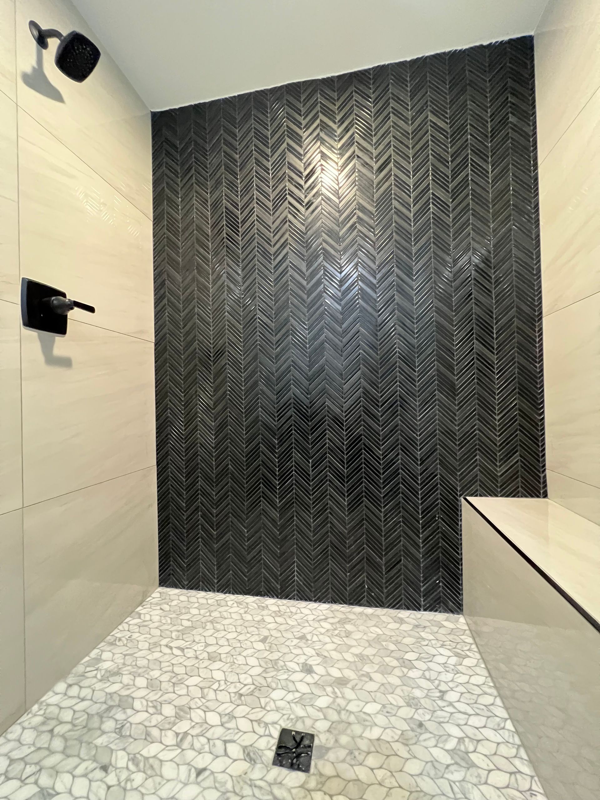 A shower with a black and white tile wall and a bench.