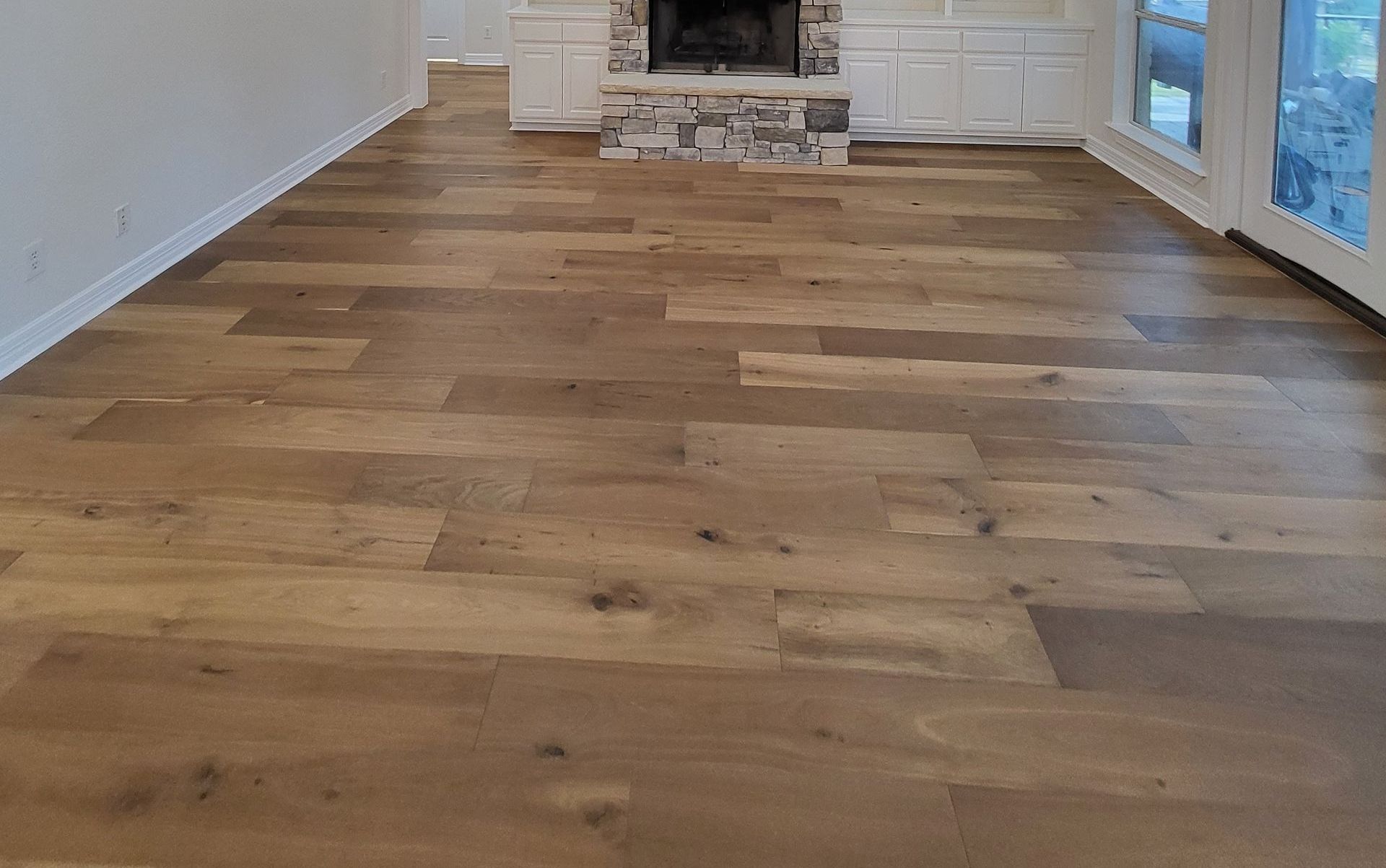 Wooden floorboards in a living room, leading to a fireplace and large windows.