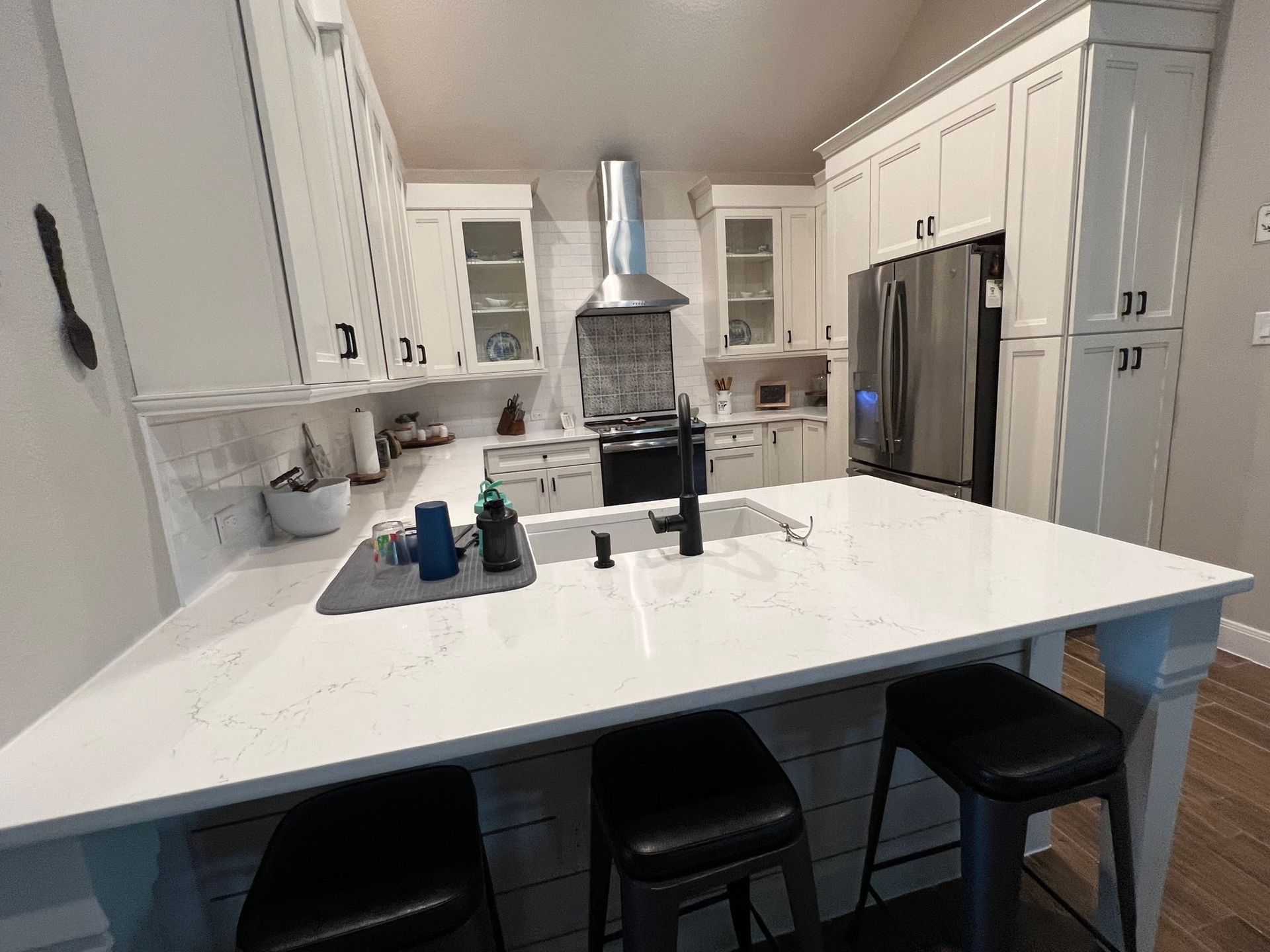 A kitchen with white cabinets , stainless steel appliances , a sink , and a large island.
