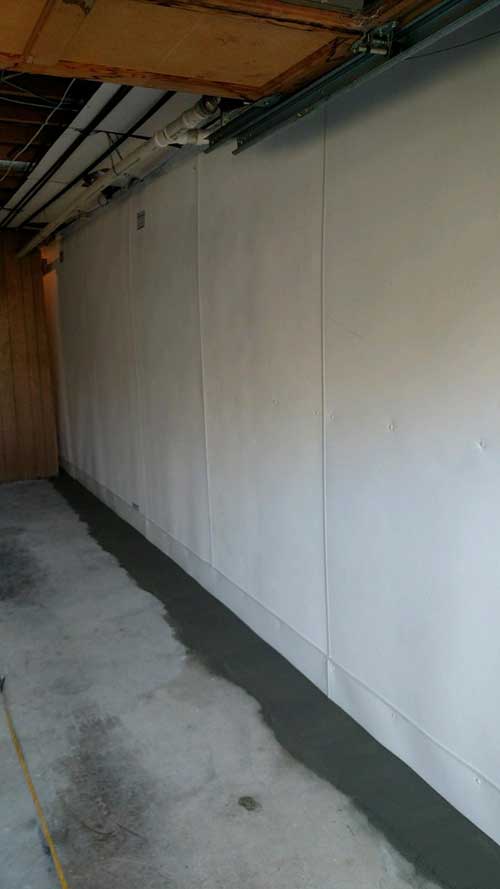 a long white wall in a basement with a concrete floor .