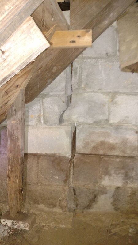 a brick wall with a  crack that has wooden beam hanging from it .