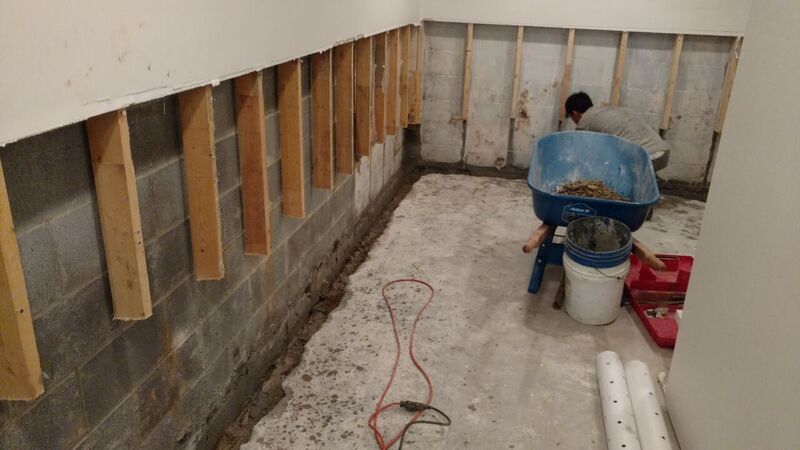 a man is working on a basement wall preparing for waterproofing system to be installed