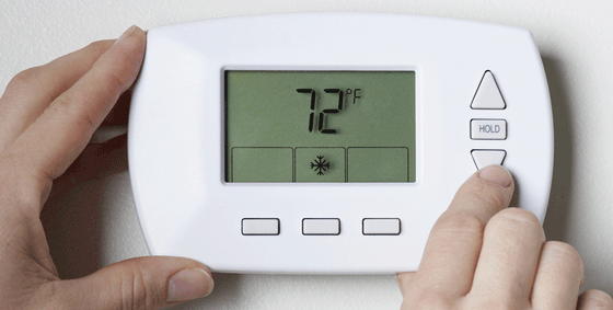 A person is holding a thermostat that shows the temperature is 72 degrees fahrenheit.