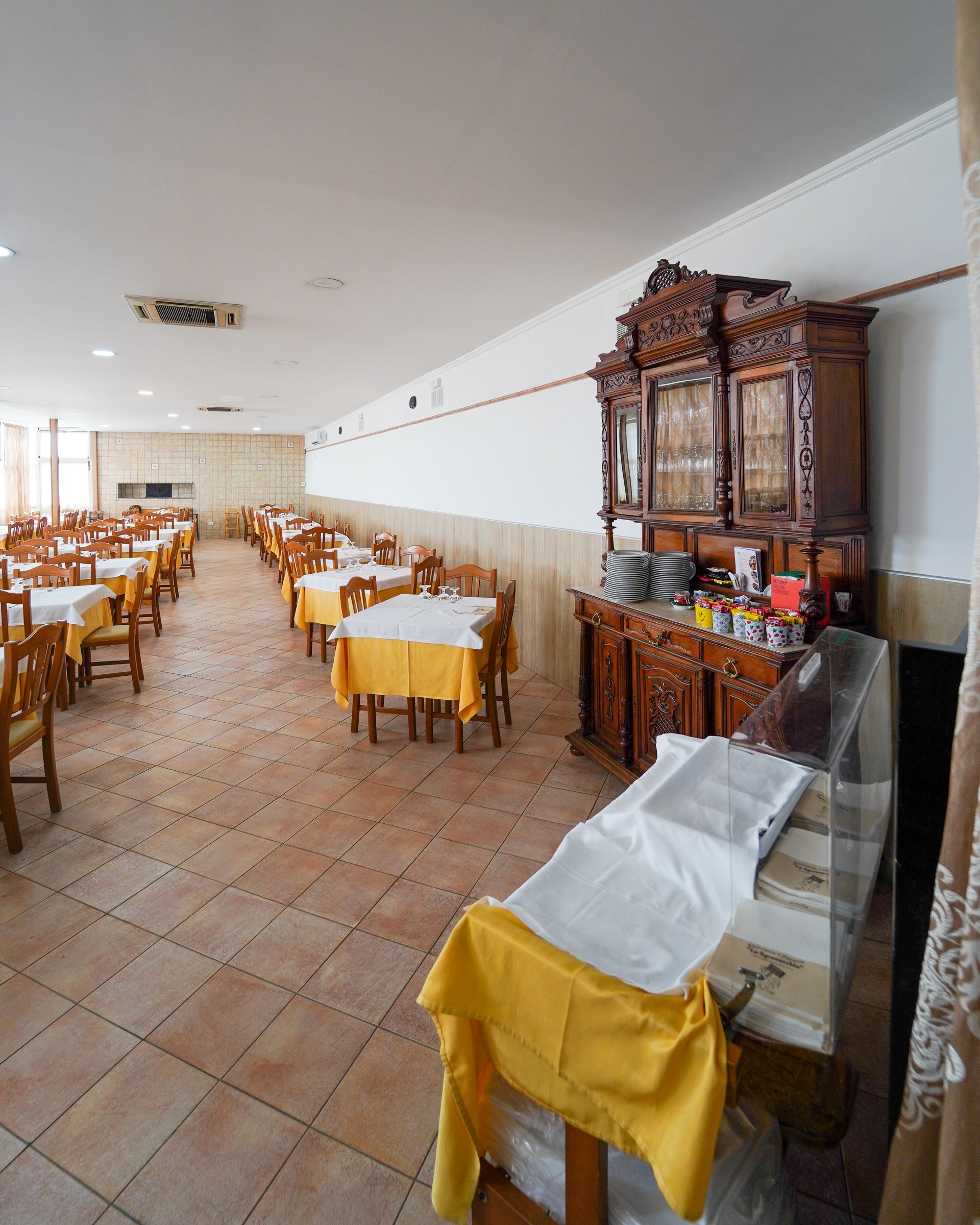 Sala da pranzo vuota con tovaglie gialle e un armadio in legno decorato lungo la parete.