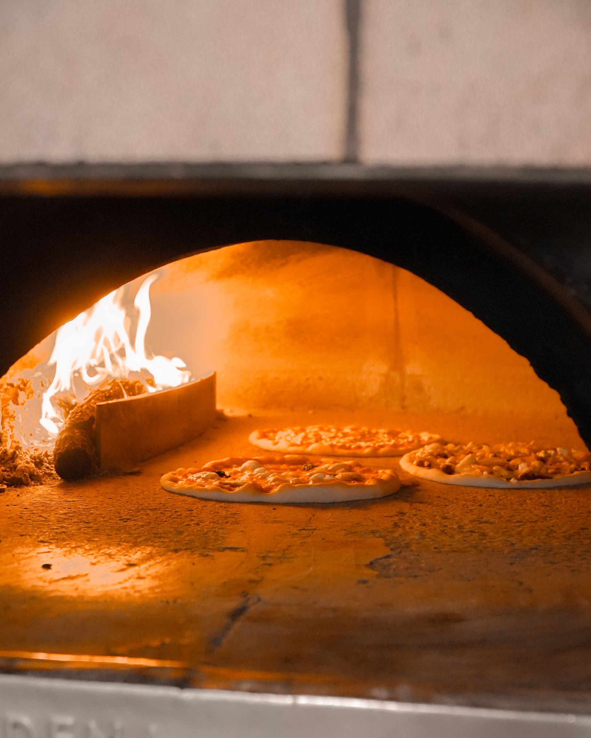 Pizza baking in a wood-fired oven with flames and an orange glow
