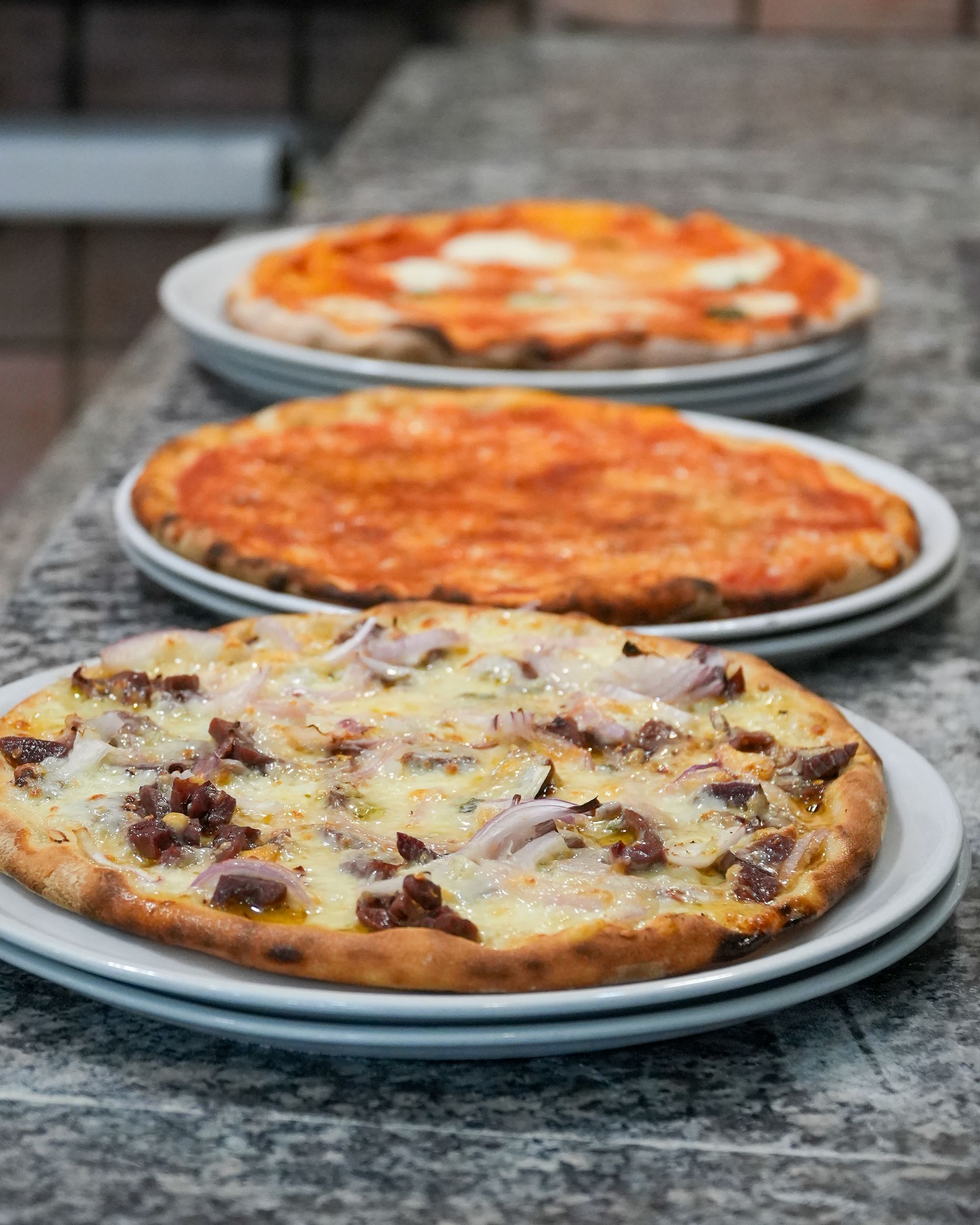 Three pizzas on plates on a granite countertop, with a mushroom pizza in the foreground