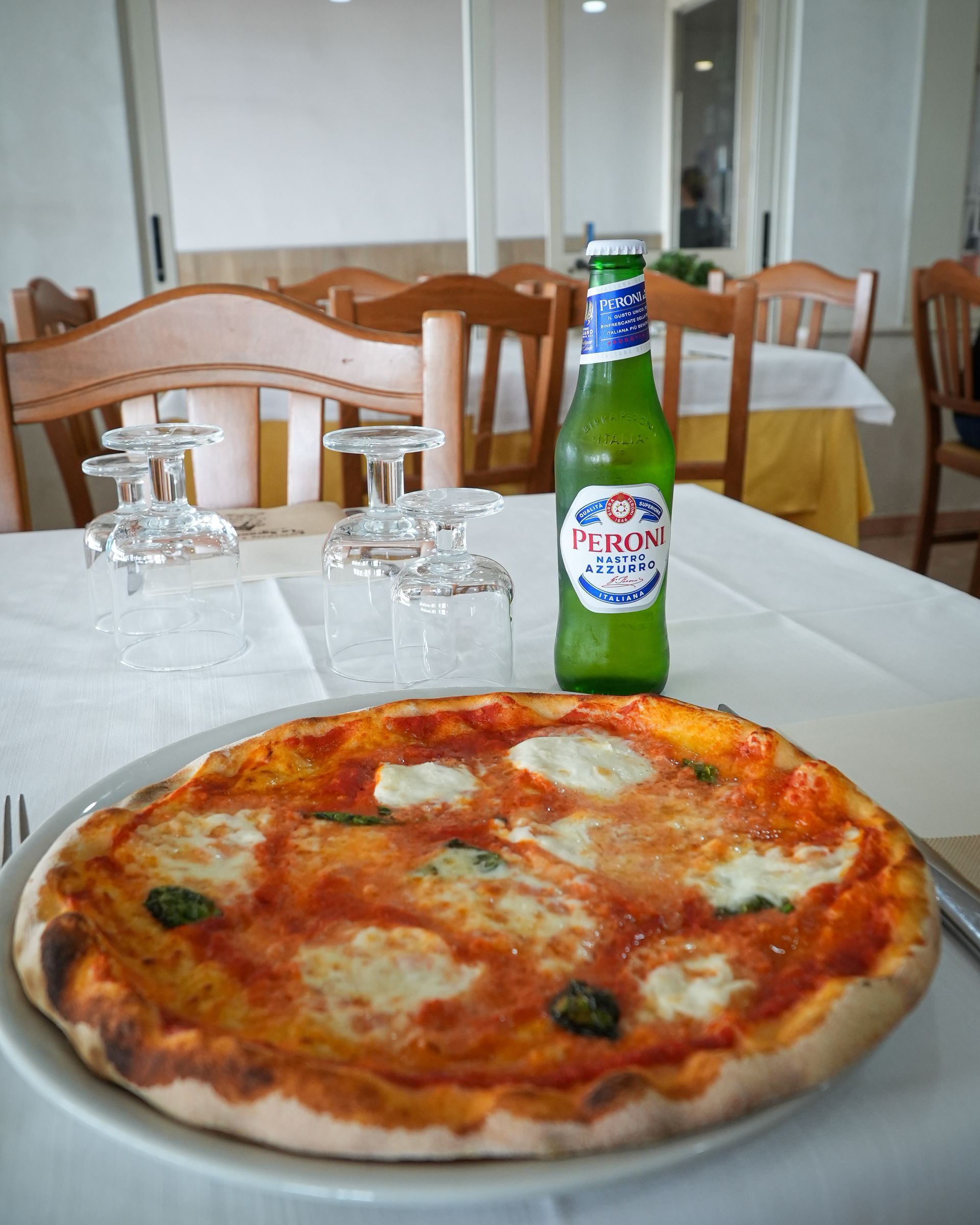 Pizza on a plate with a green beer bottle on a restaurant table.