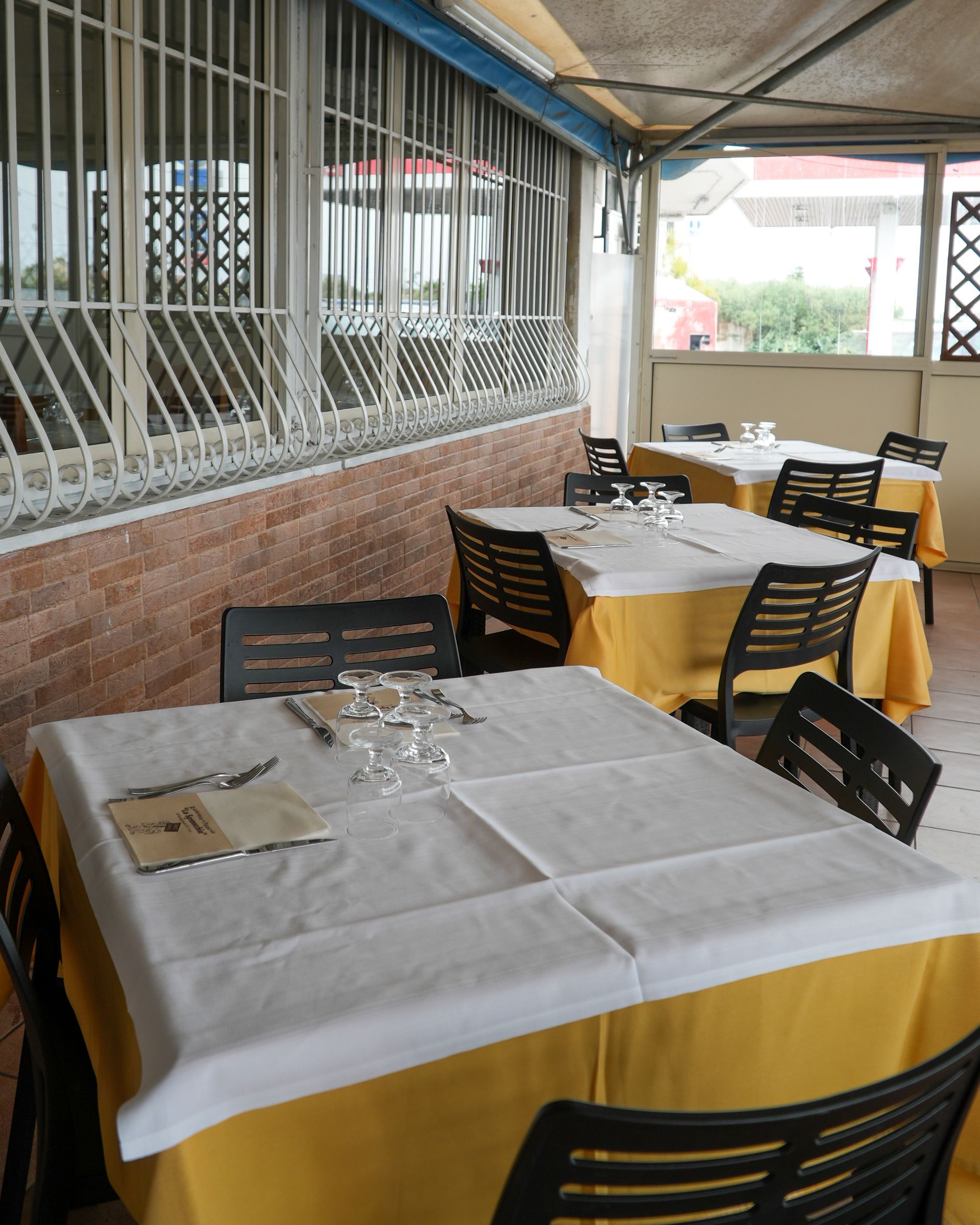 Tavoli all'aperto del ristorante con tovaglie gialle e sedie nere sotto un patio coperto.