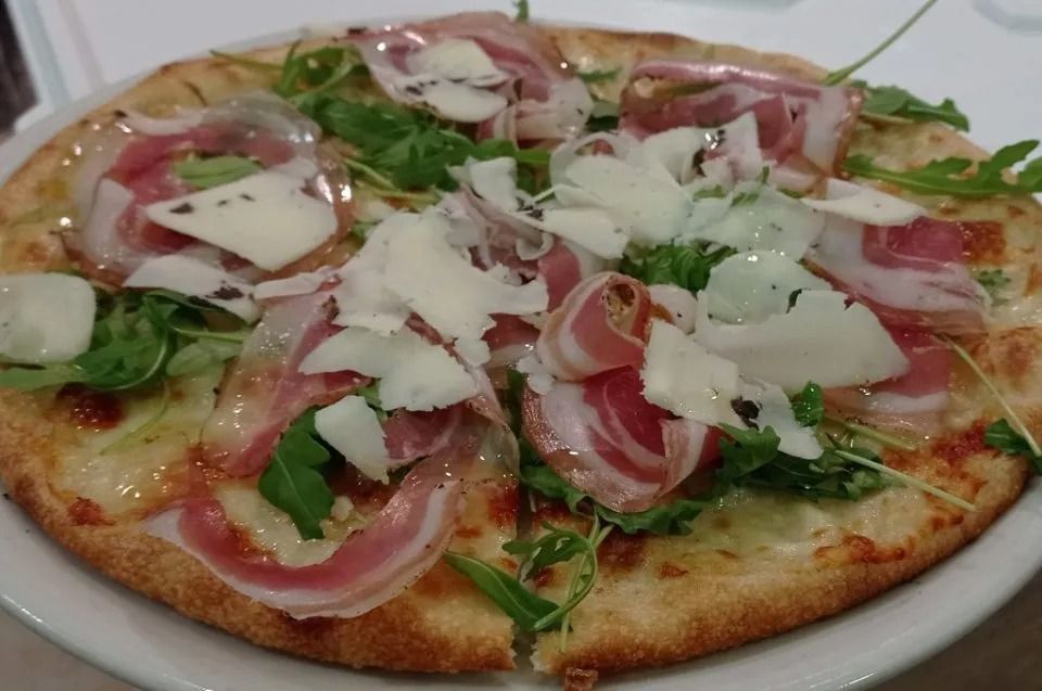 Pizza topped with prosciutto, arugula, and shaved cheese on a white plate